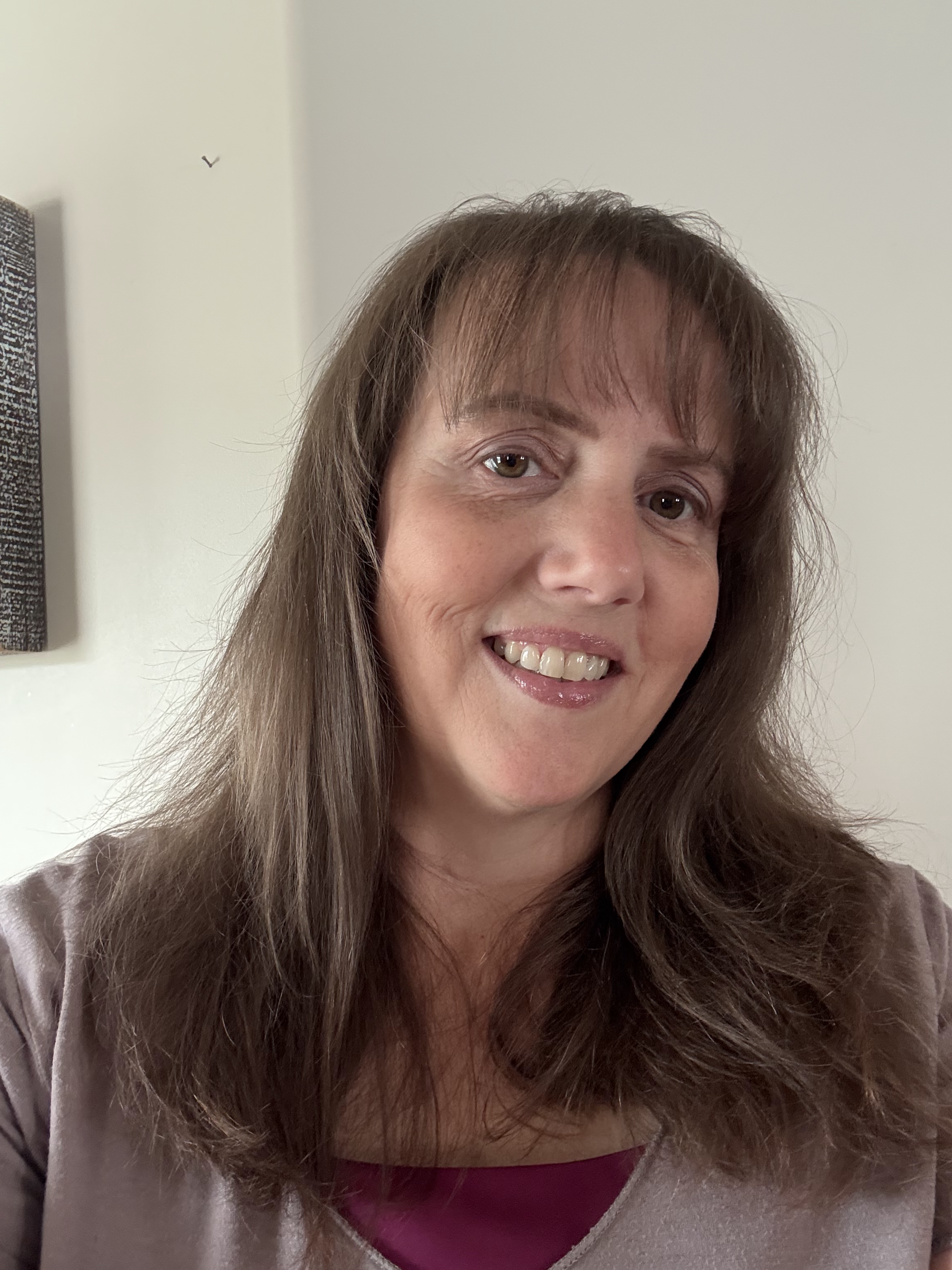 Woman with shoulder-length brown hair smiling in front of a white wall.